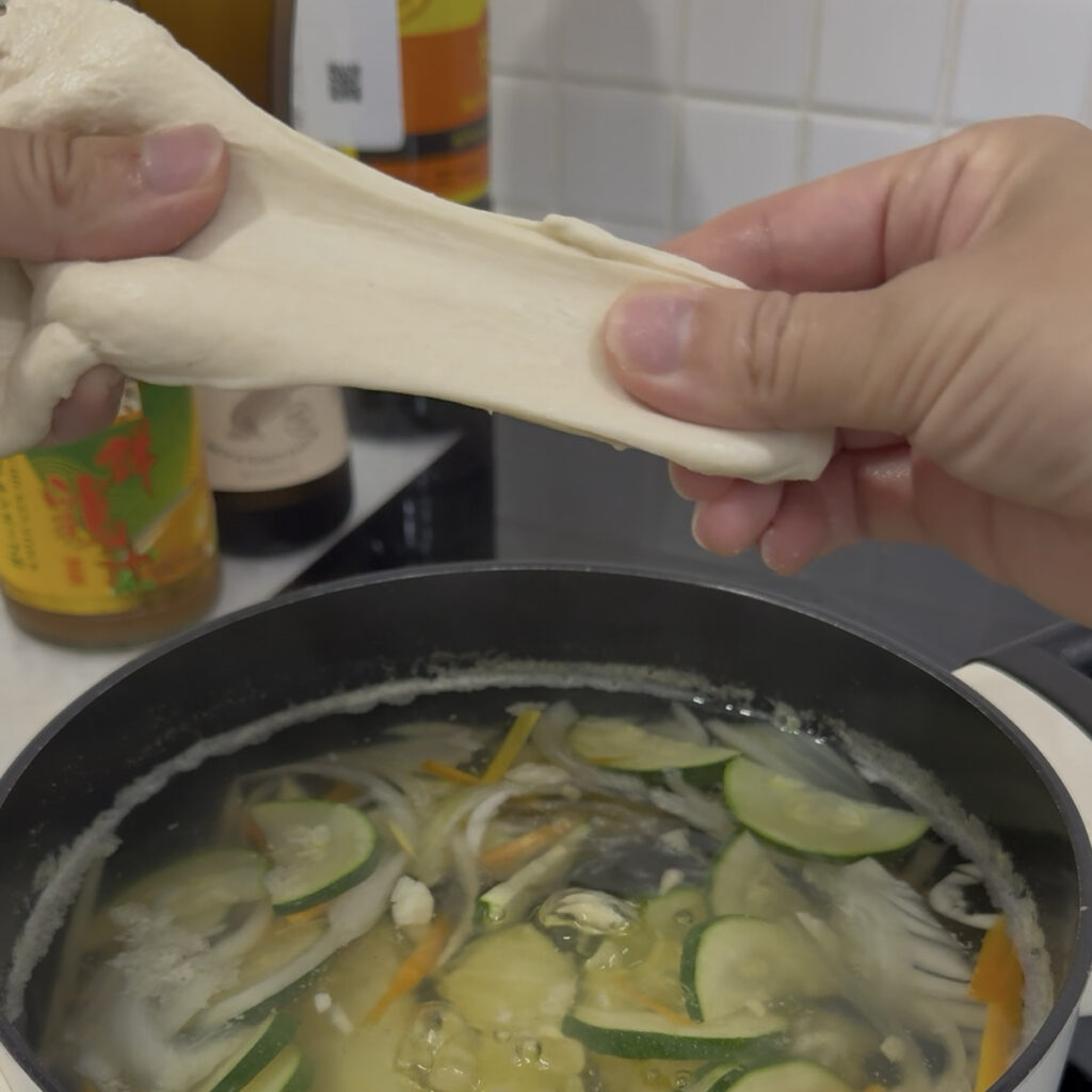 Sujebi Korean sujebi dough being stretched and prepared over vegetable soup