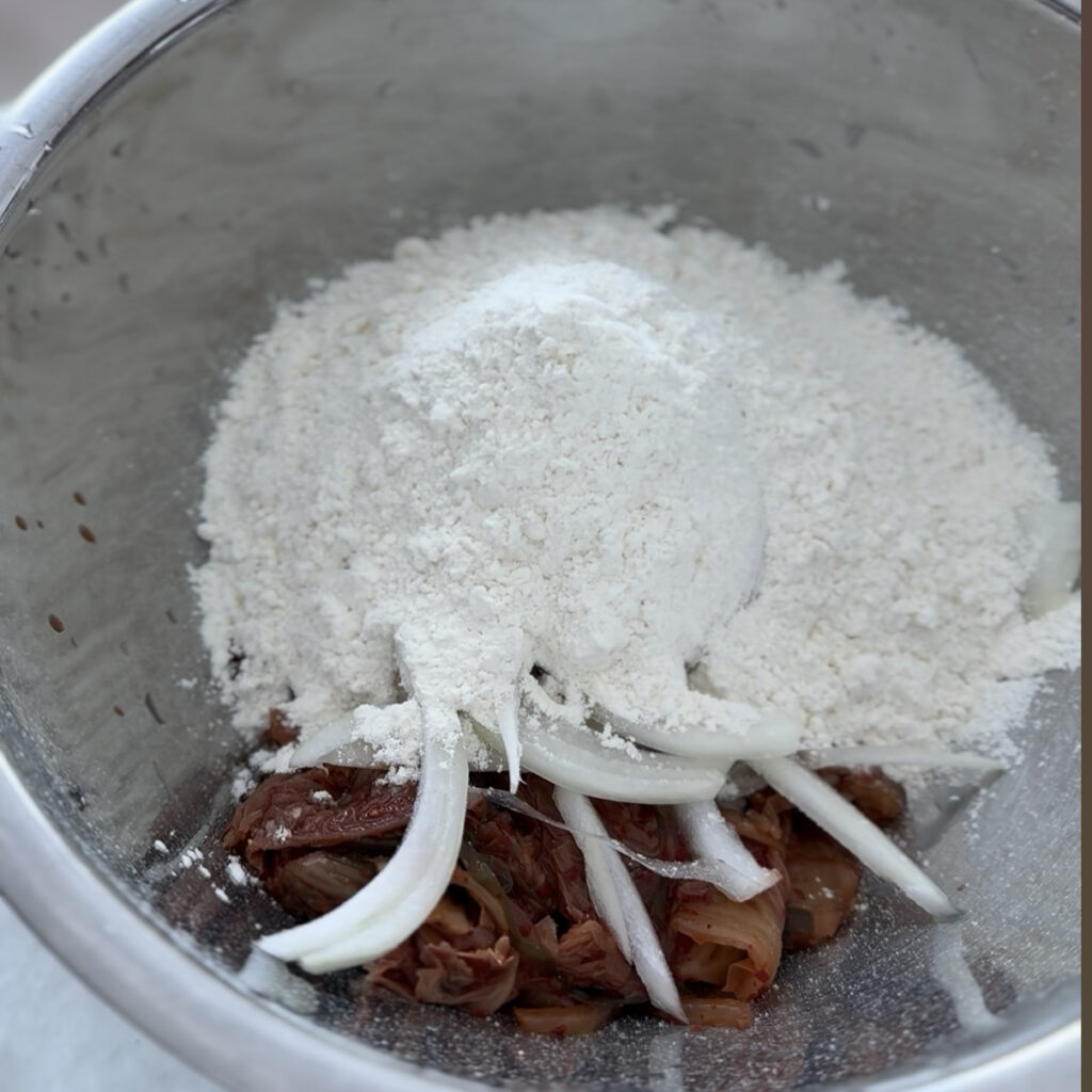 Sour kimchi, onion, and pancake mix in a bowl before mixing