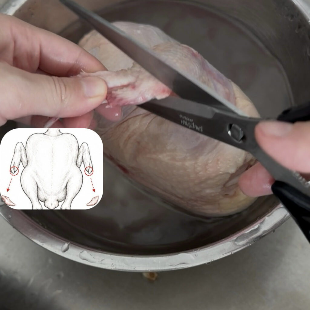 Trimming the wing tips of a whole chicken using kitchen shears.
