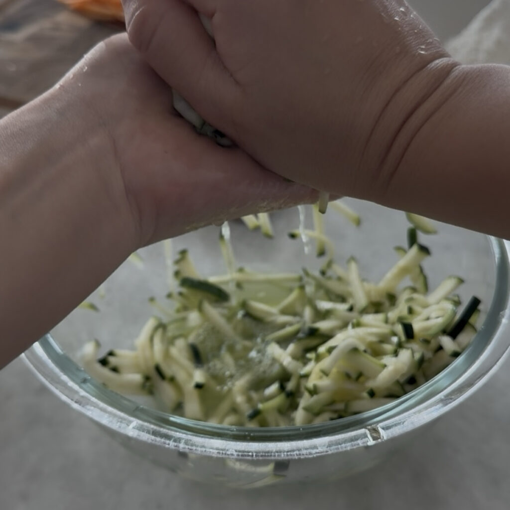 Squeezing excess moisture from julienned zucchini using a clean kitchen towel for crispy Korean zucchini pancakes.