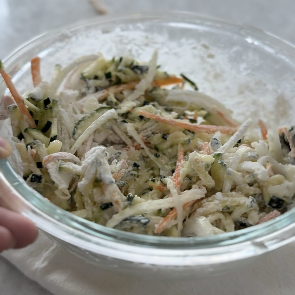 Mixing zucchini, onion, carrot, Korean pancake mix, and potato starch in a large bowl.