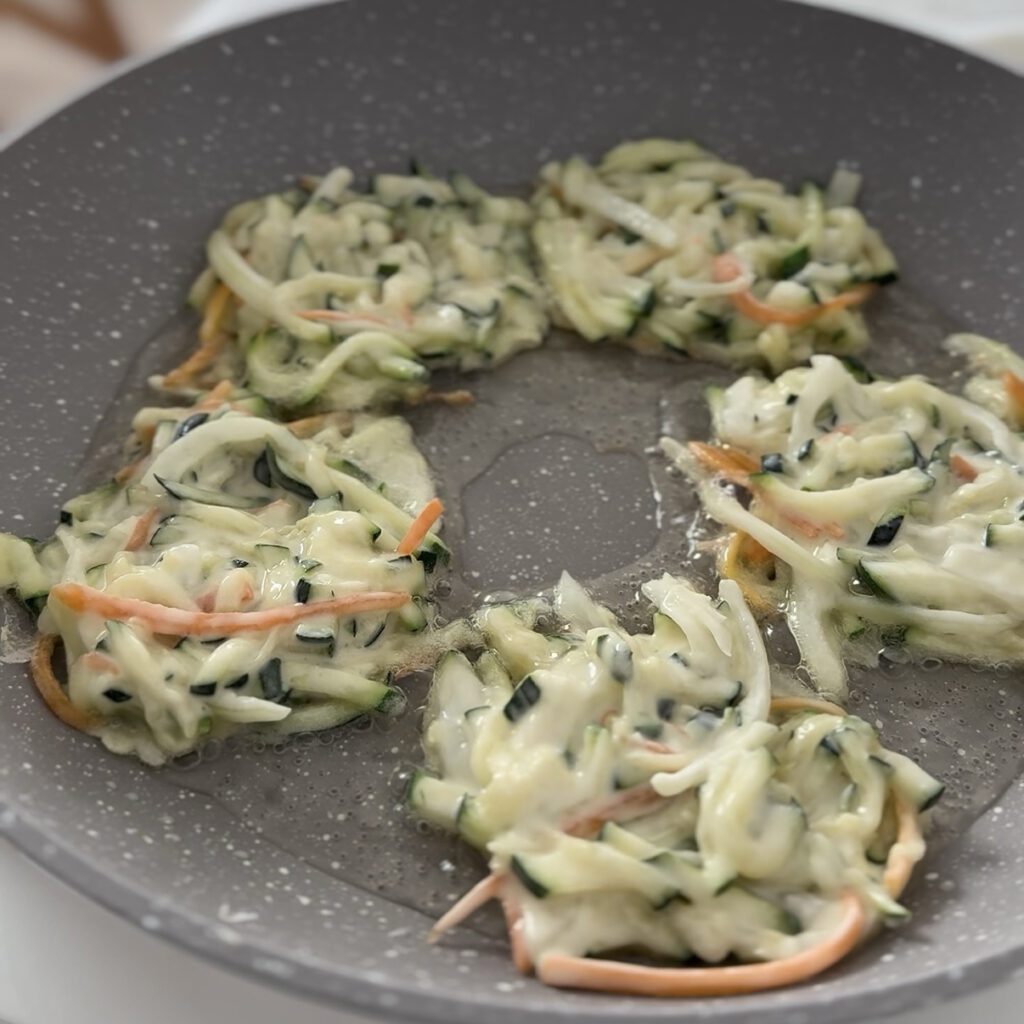 Cooking Korean zucchini pancake in a skillet until the bottom is golden brown and crispy.