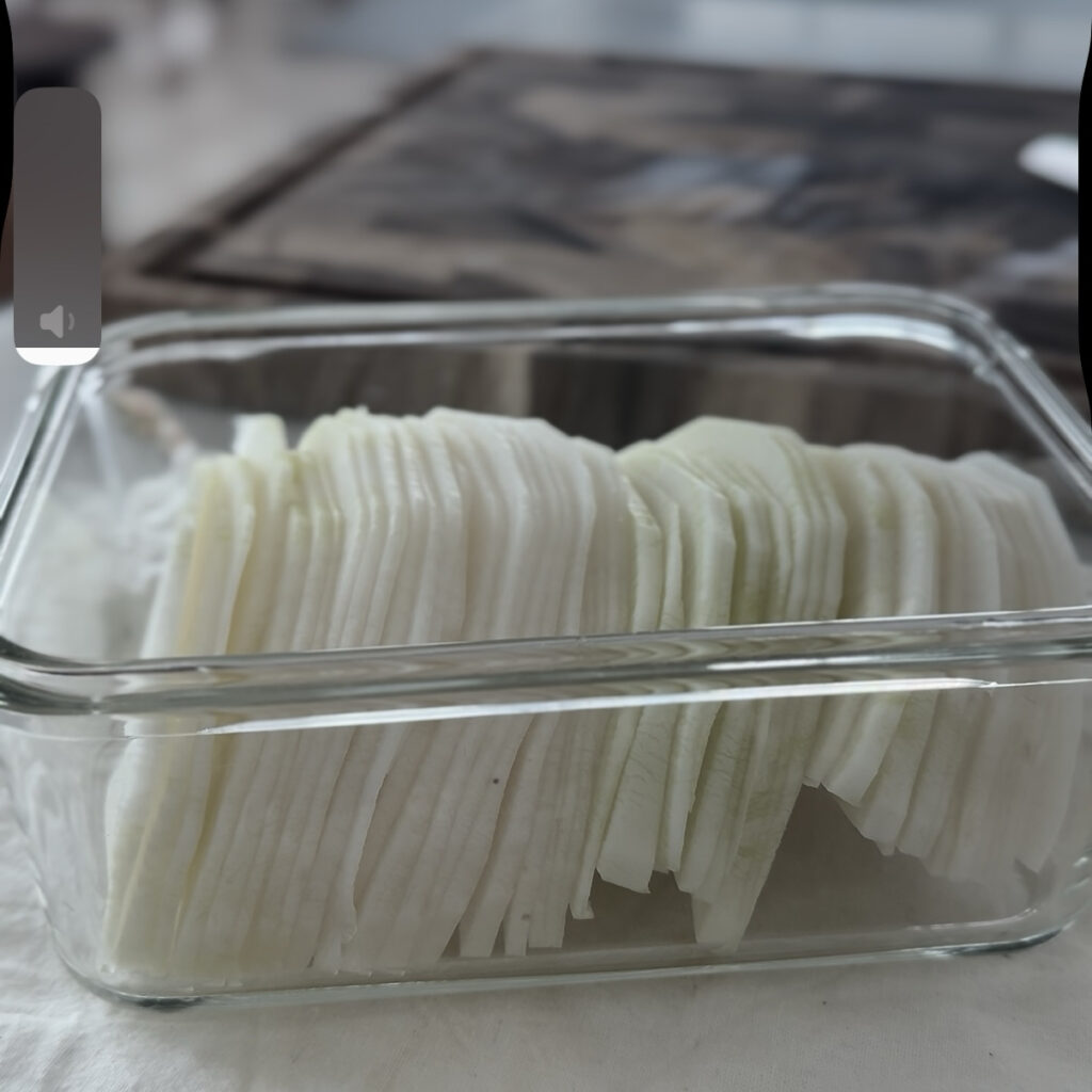 Thinly sliced daikon radish in a glass container, ready for pickling.
