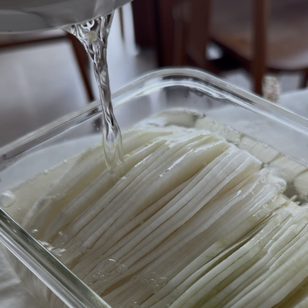 Freshly made pickling liquid being poured over sliced daikon radish.