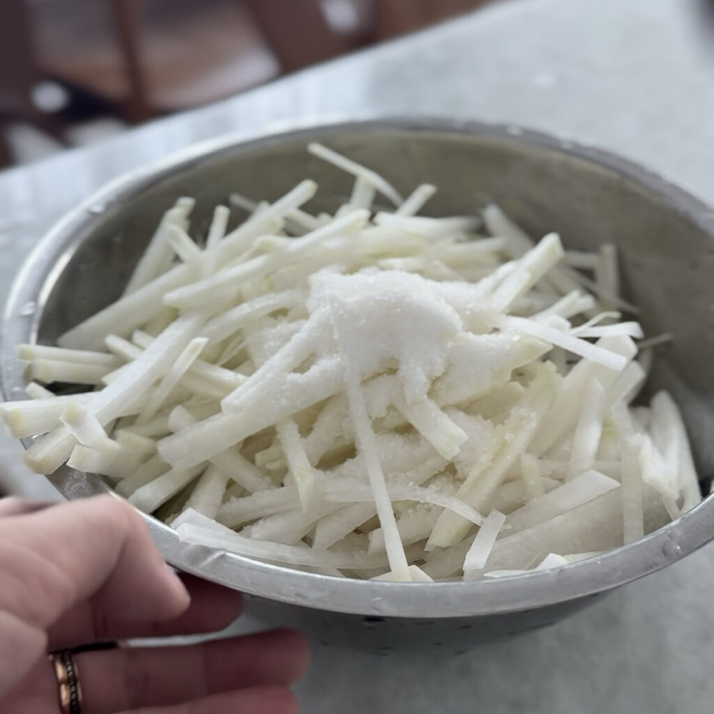 Julienned daikon radish mixed with salt and sugar before seasoning.