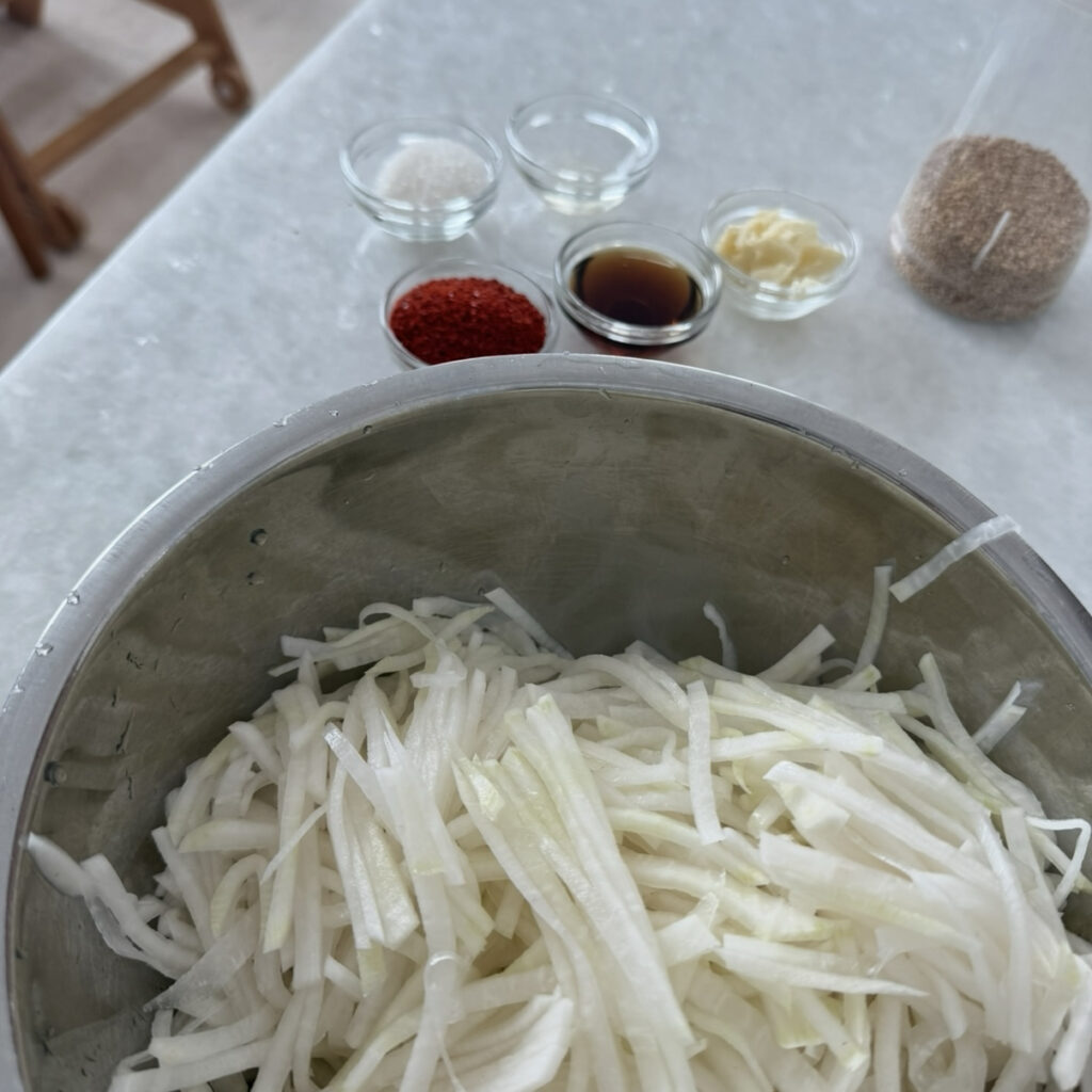 Ingredients for Korean Spicy Radish Salad (Musaengchae), including daikon radish, gochugaru, fish sauce, garlic, sugar, vinegar, sesame seeds, and green onion