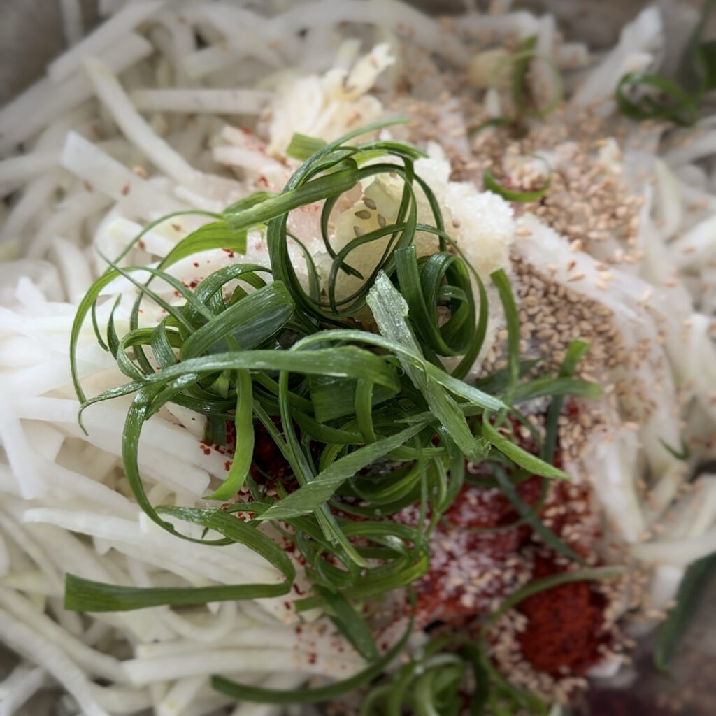 Ingredients for Korean spicy radish salad, including gochugaru, fish sauce, garlic, and green onions.