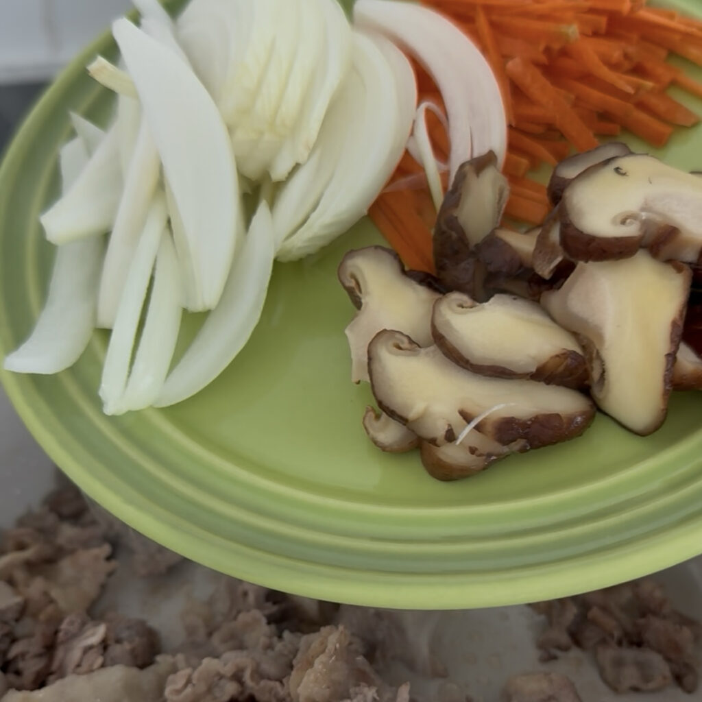 Adding onions, carrots, and shiitake mushrooms to the pan