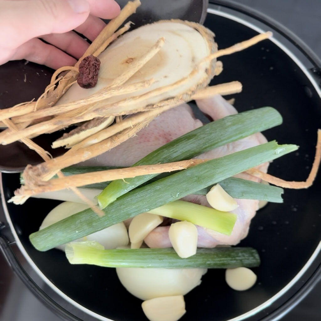 Whole chicken with garlic, onion, green onion, and herbs in a pot.