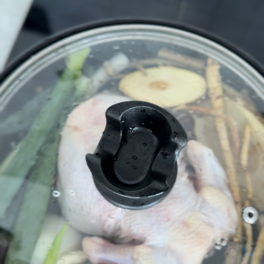 A whole chicken cooking in a pot with garlic, onion, and herbs for Samgyetang.