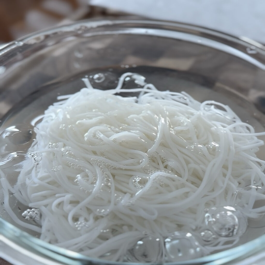 Cooked noodles being rinsed under cold running water to remove excess starch.