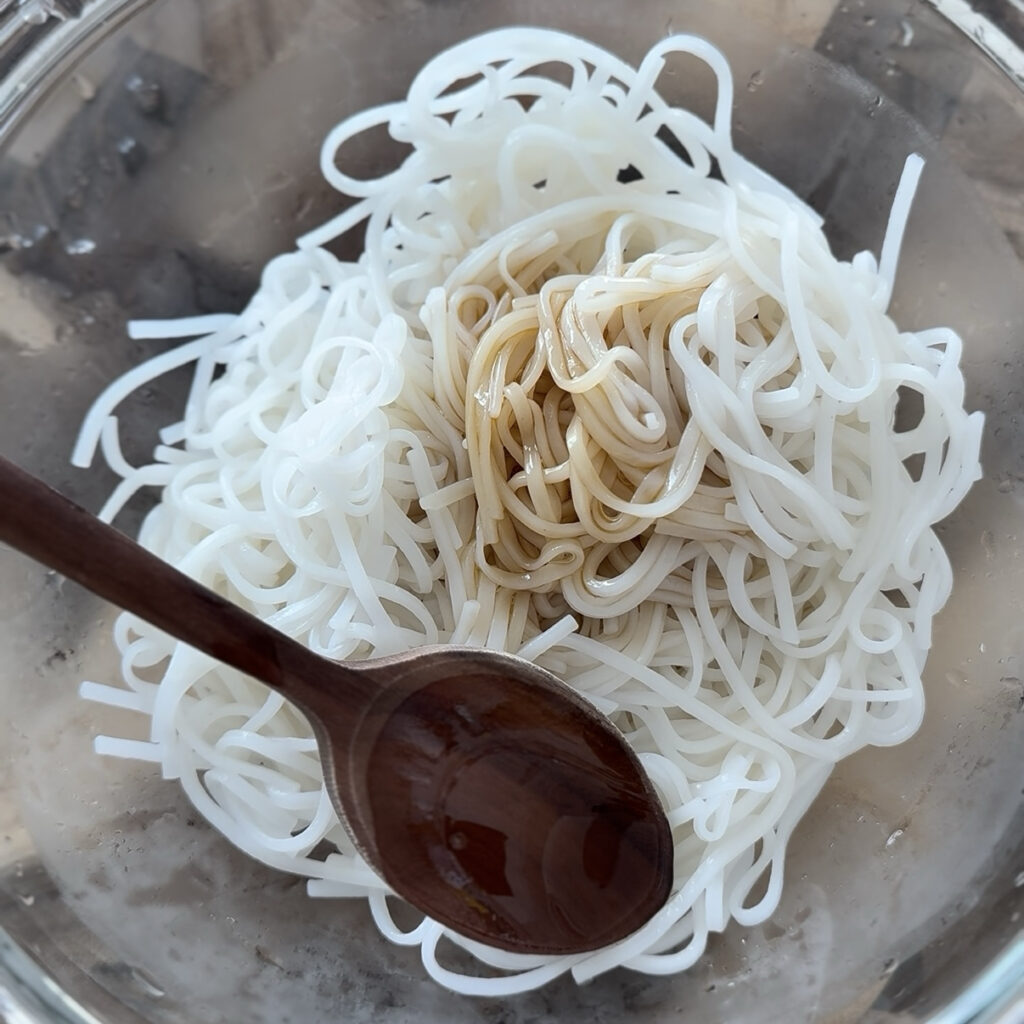 Perilla oil, Korean soy sauce, and sugar being mixed with the cooked noodles.
