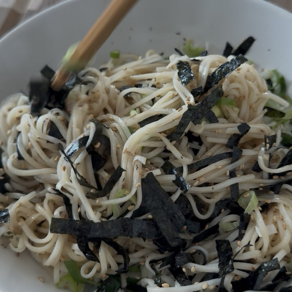 Mixing the noodles with the toppings before serving.