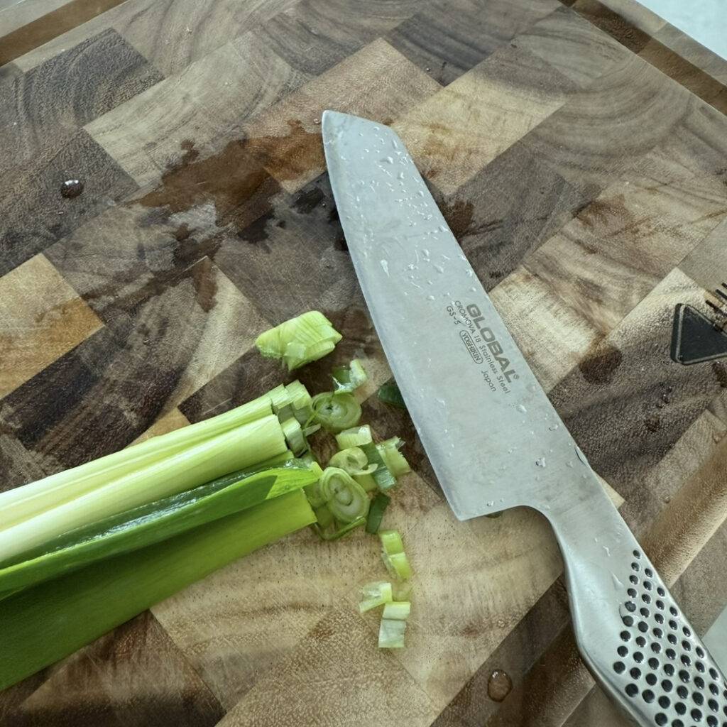 Green onion being thinly sliced for Korean Perilla Oil Noodles.