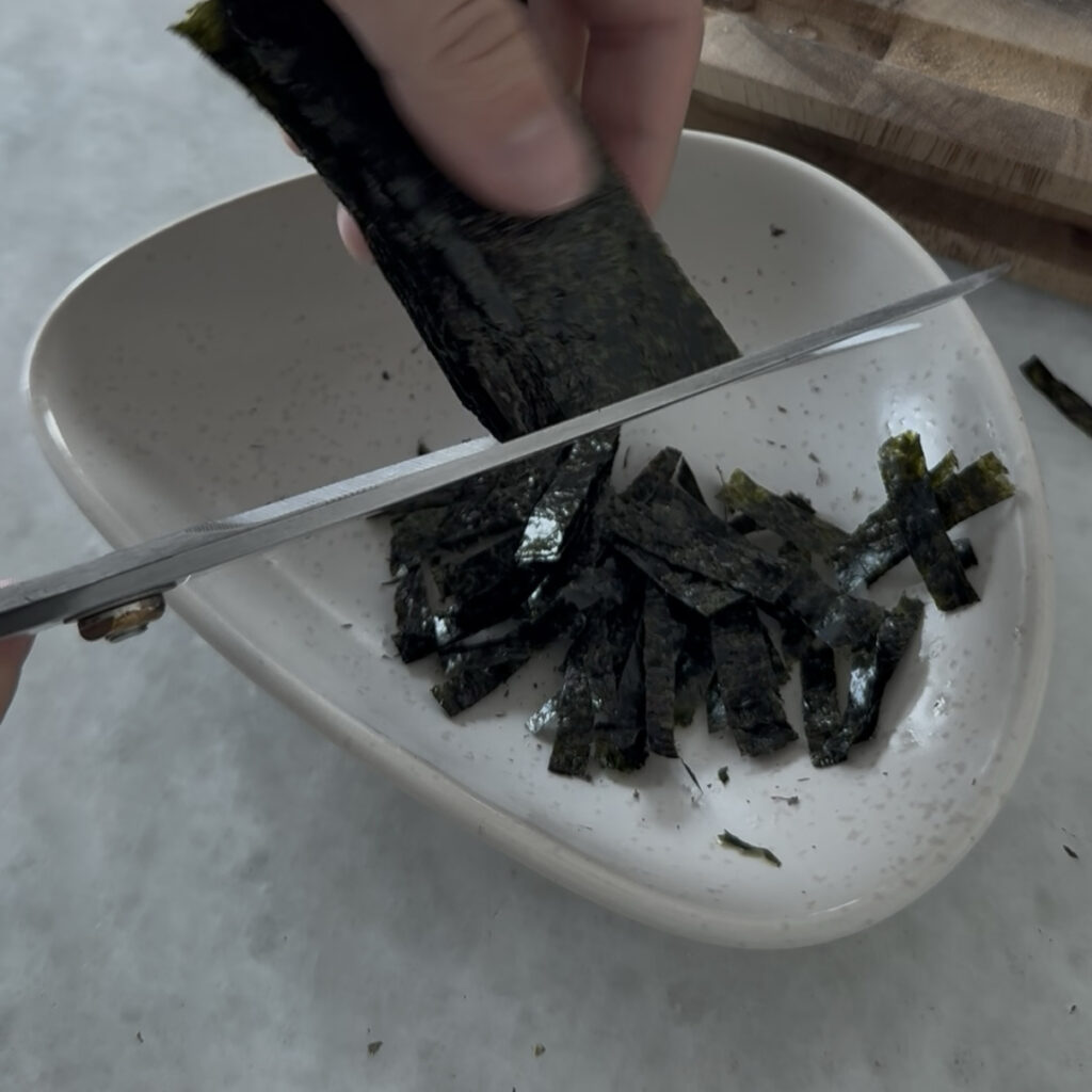 Roasted seaweed being cut into thin strips with kitchen scissors.