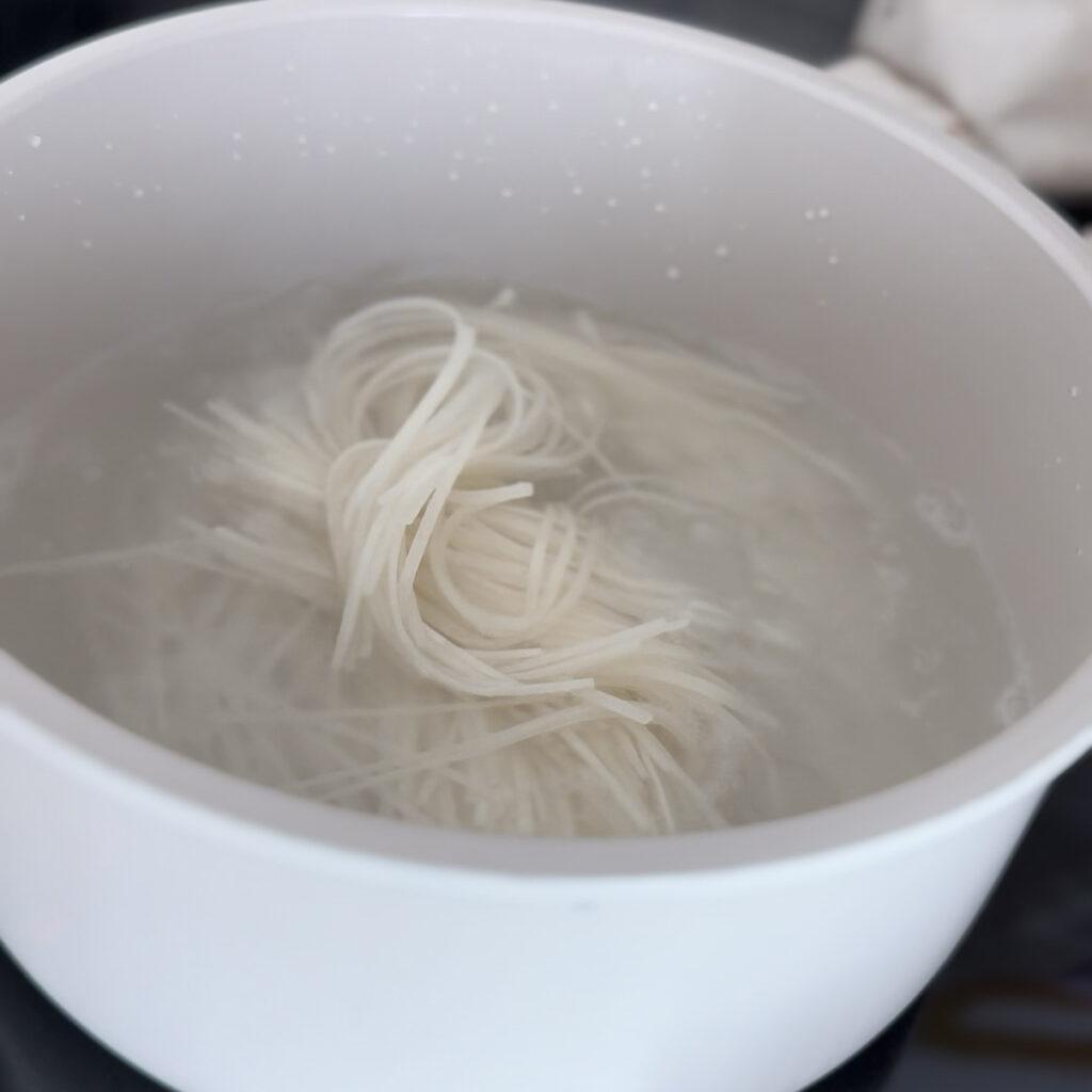 Thin wheat noodles cooking in a pot of boiling water.