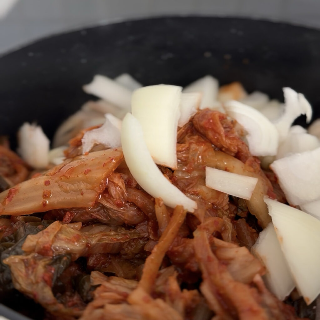 Kimchi and sliced onion cooking with pork for Kimchi Jjigae