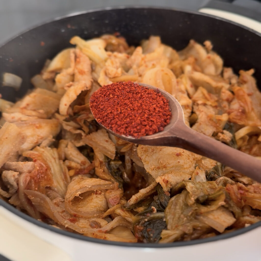 Adding gochugaru to sautéed kimchi and pork