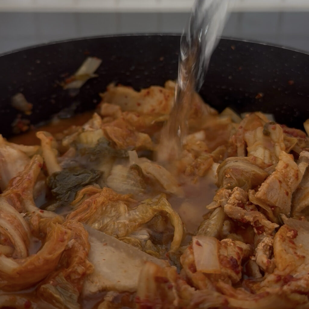 Adding water to the kimchi and pork mixture for Kimchi Jjigae