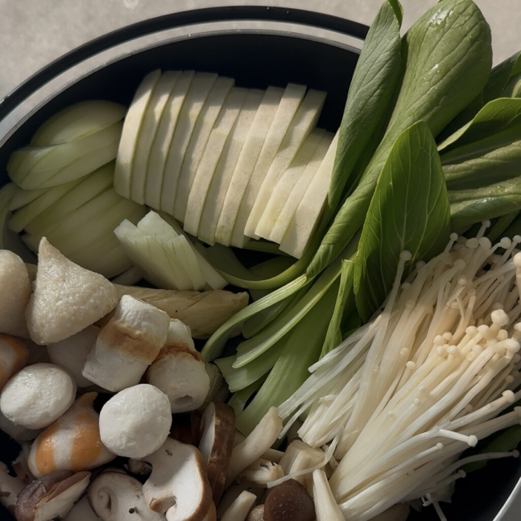 Fresh vegetables, mushrooms, and fishballs arranged in a hot pot before cooking.