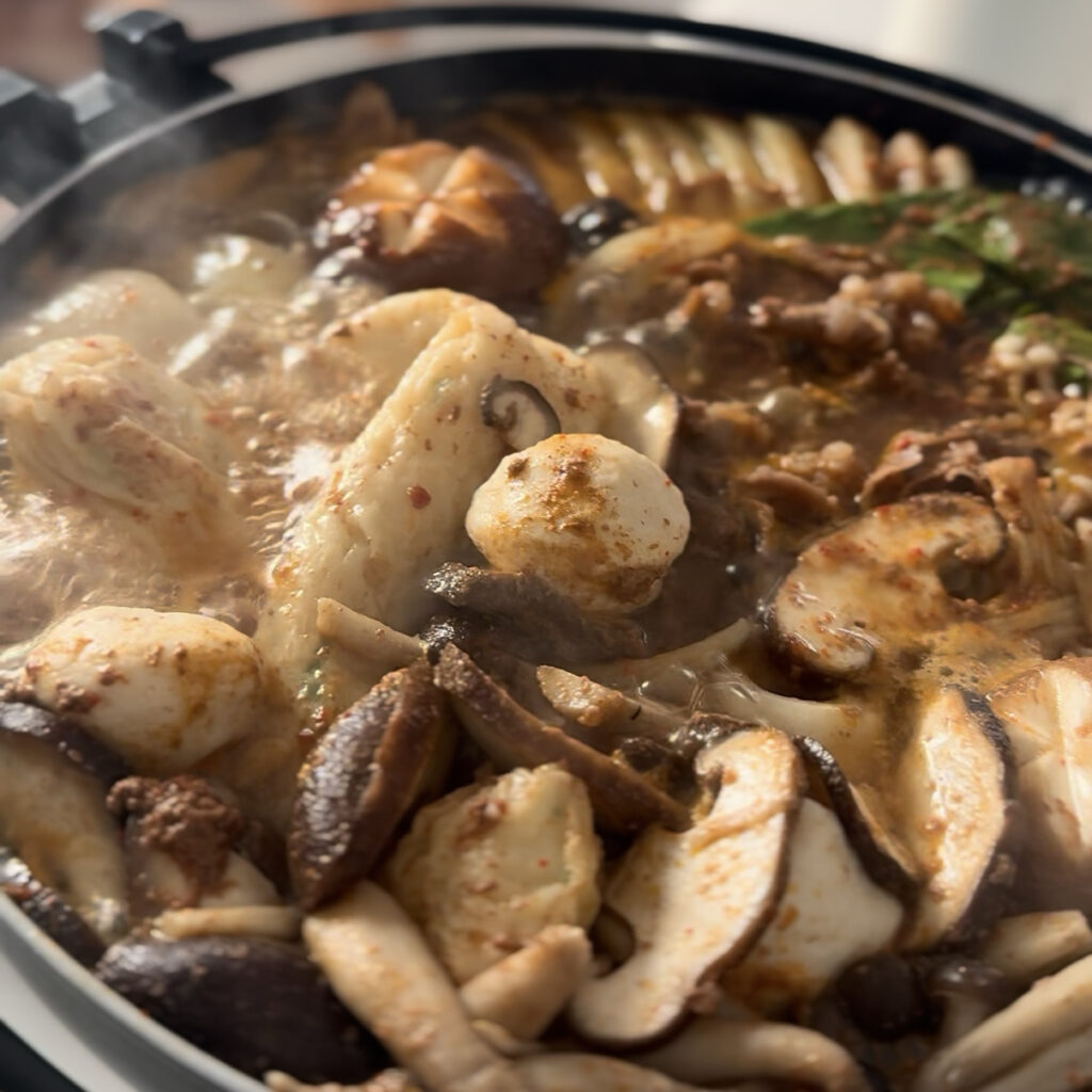 A bubbling pot of homemade Korean spicy shabu shabu loaded with beef, mushrooms, and fresh vegetables.