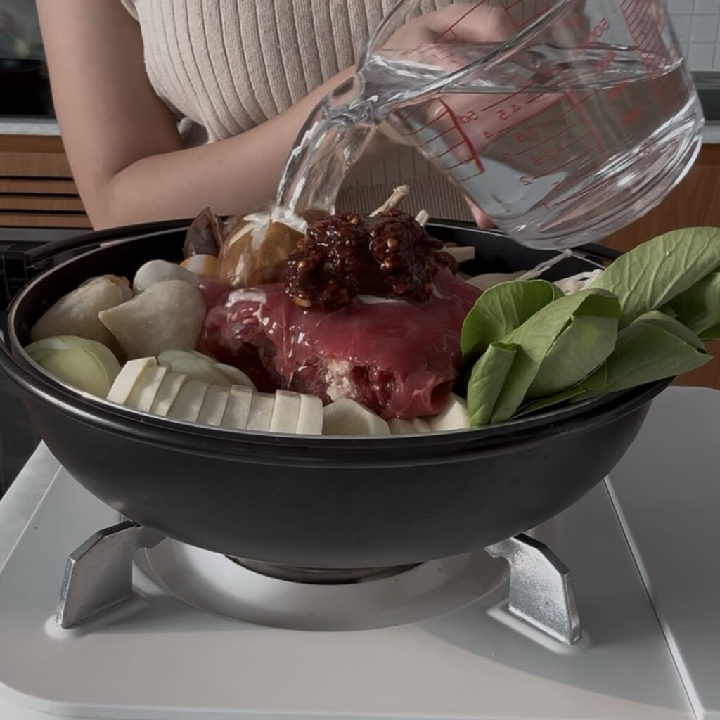 Pouring water into the pot over the shabu shabu ingredients before cooking.