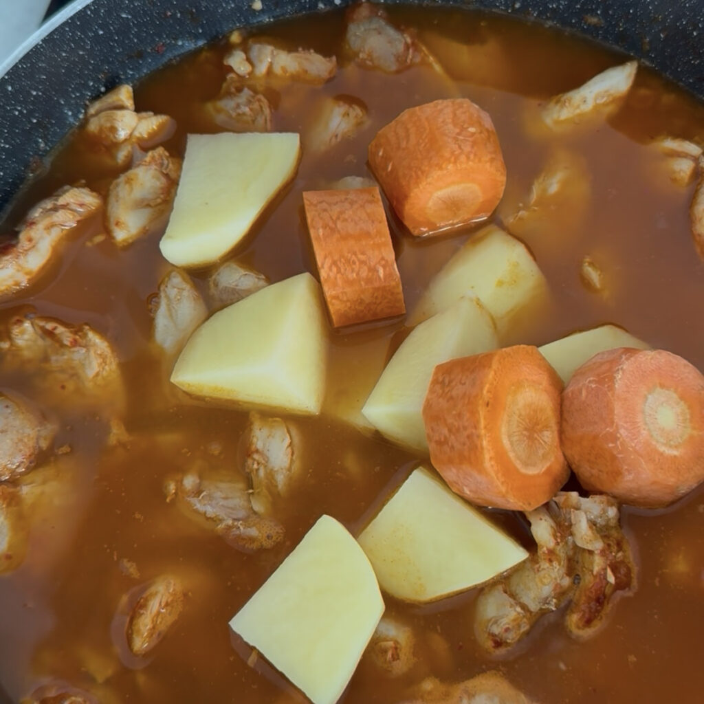 Chicken thighs simmering with potatoes and carrots in a spicy Korean sauce.