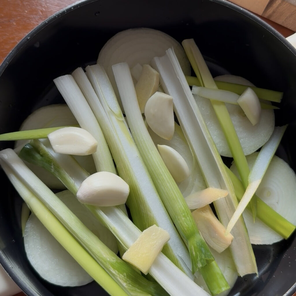 Layering onion, green onion, garlic, and ginger in a pot