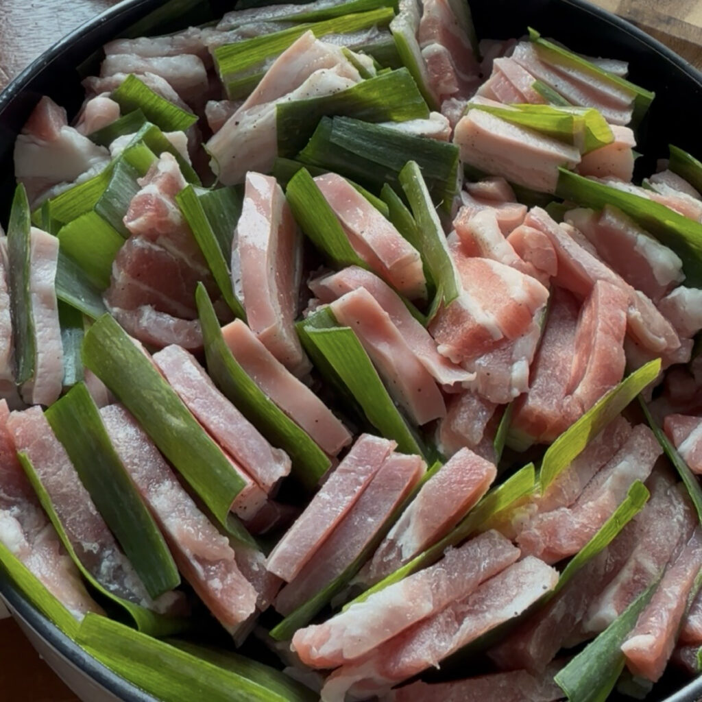 Placing the pork and green onion pieces over the vegetables