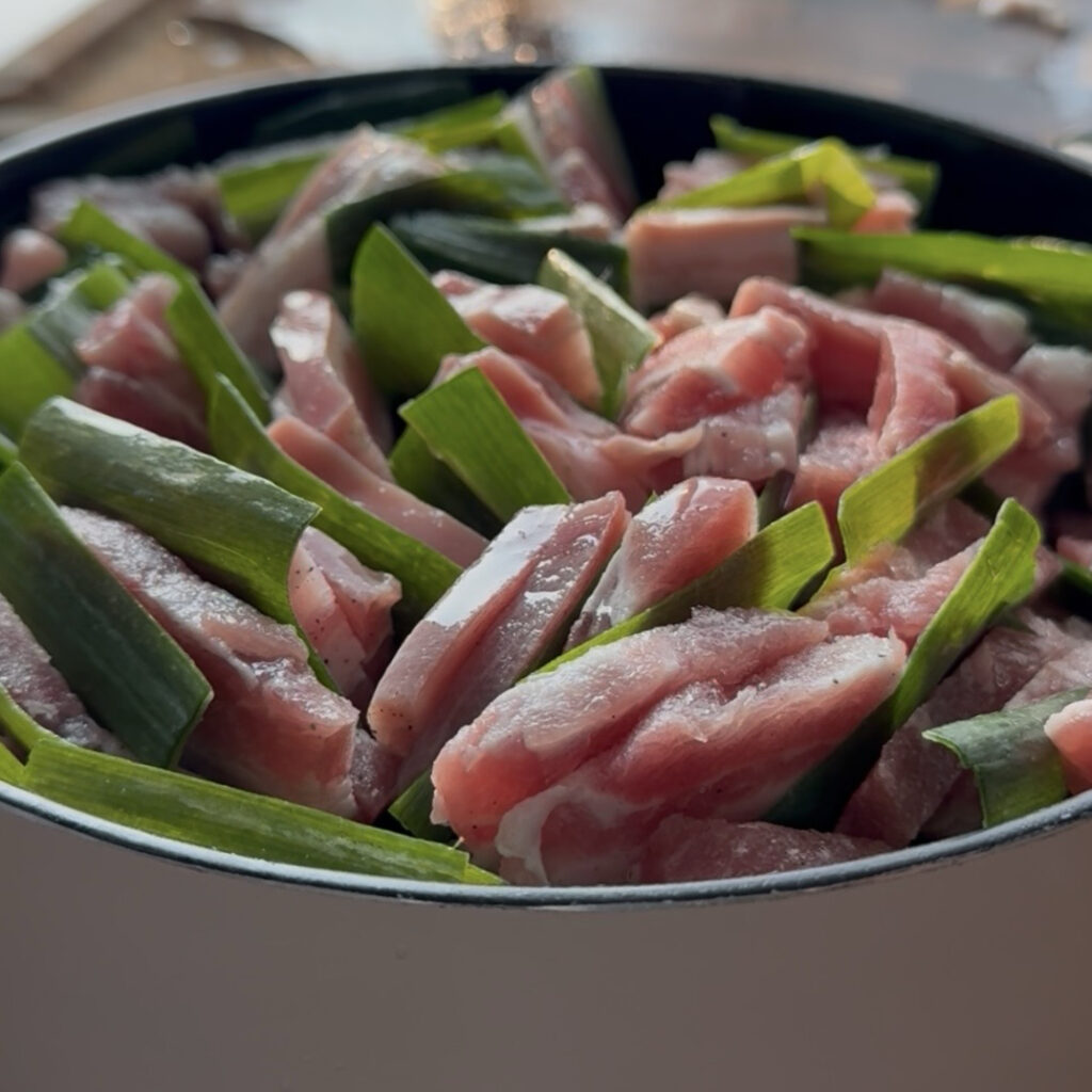 Sliced pork belly and green onions arranged over onion, garlic, and ginger