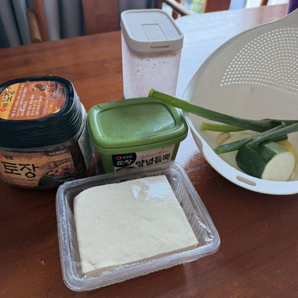 Ingredients for Korean BBQ-style doenjang jjigae, including doenjang, ssamjang, potato, zucchini, onion, tofu, and green onion