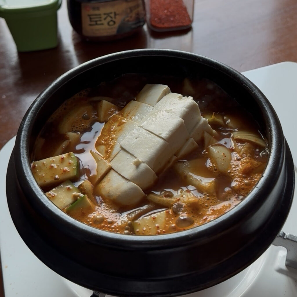 Adding potato, zucchini, onion, and tofu to doenjang jjigae