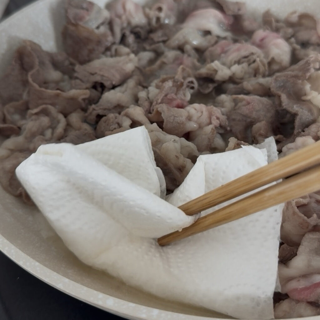 Removing excess fat from the cooked beef with a paper towel