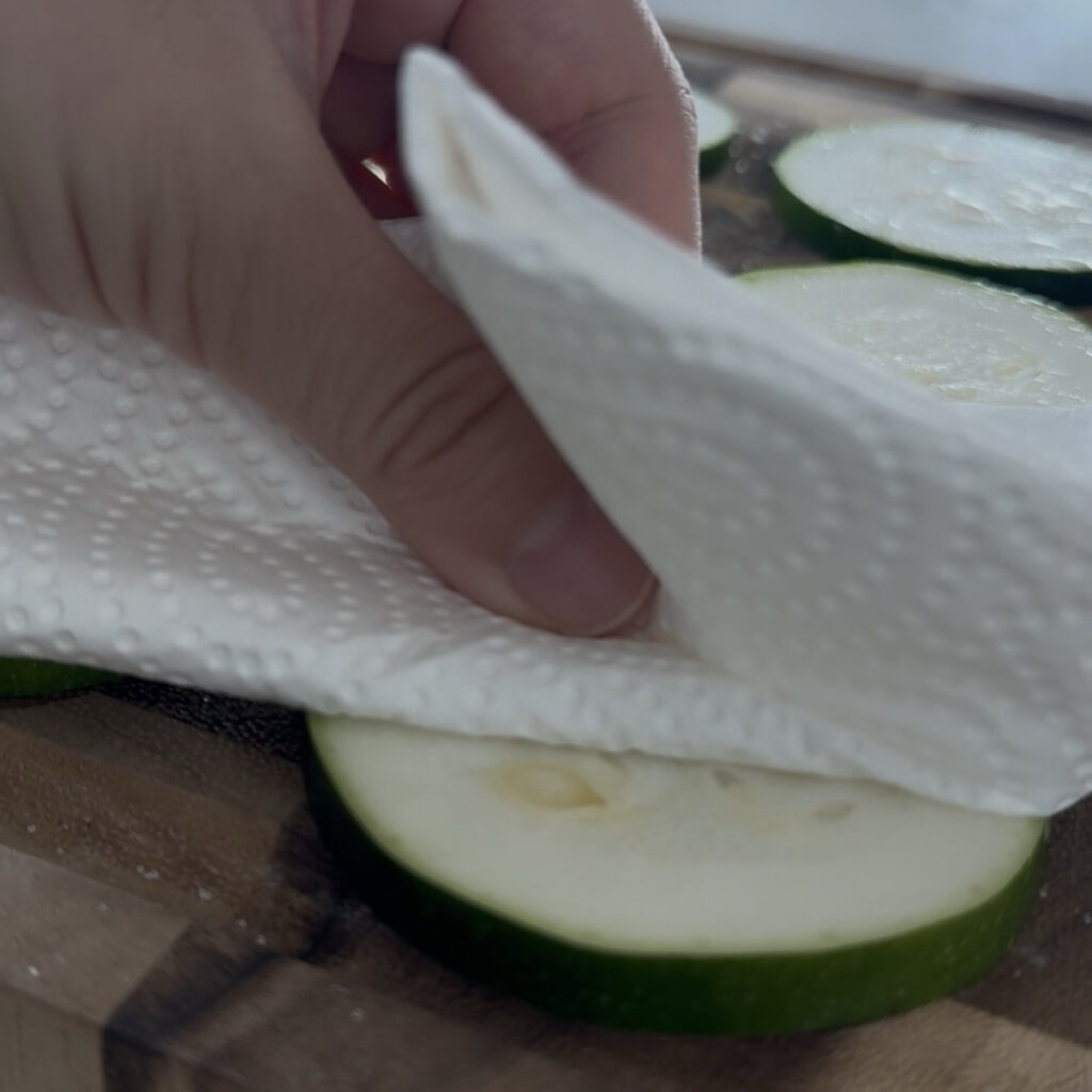 Patting salted zucchini dry with a paper towel
