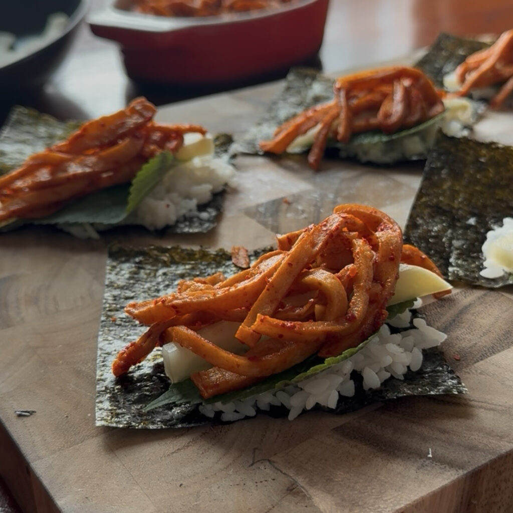 Adding rice, perilla leaves, pickled radish, and spicy fish cake to gimbap