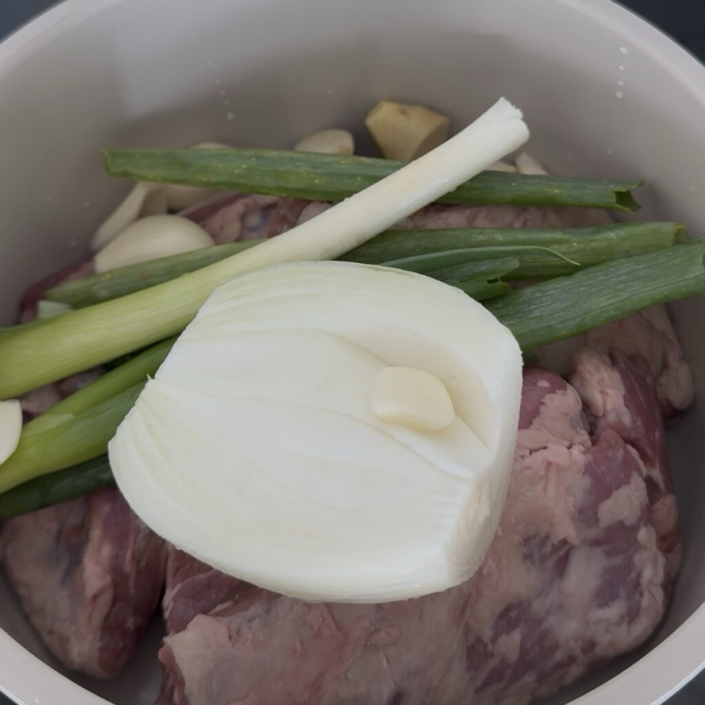 Beef with onion, green onion, garlic, and ginger in a pot
